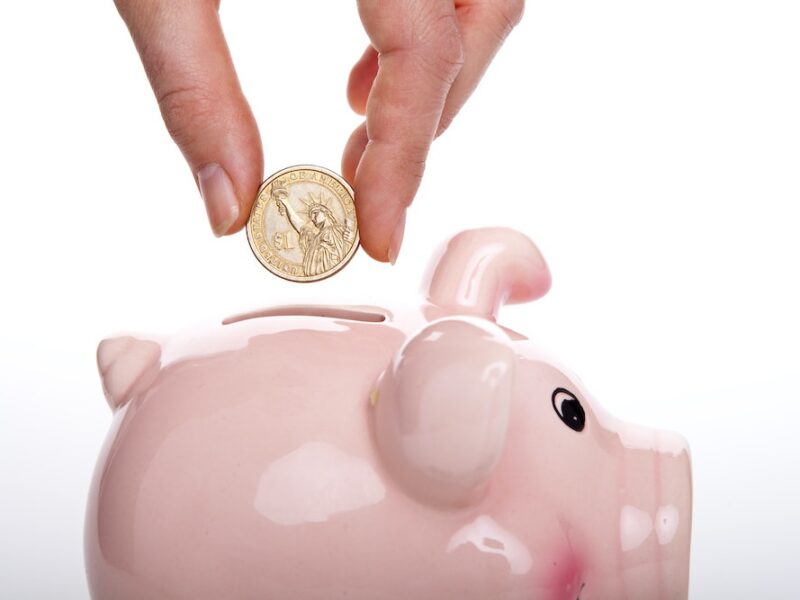 hand putting a coin into a pink piggy bank