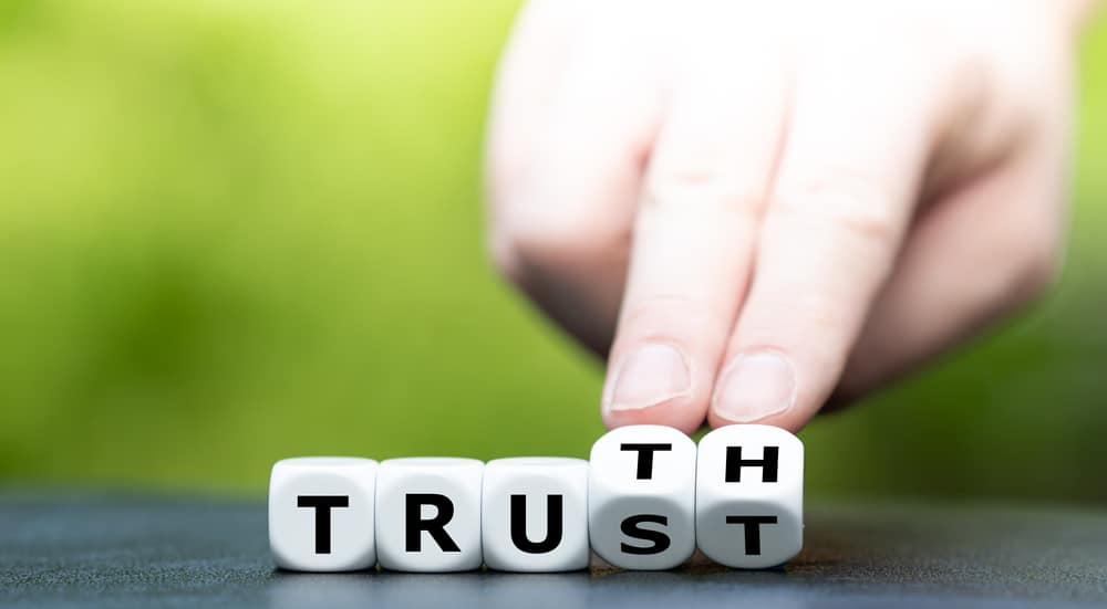 Hand turns dice and changes the word Trust to Truth.