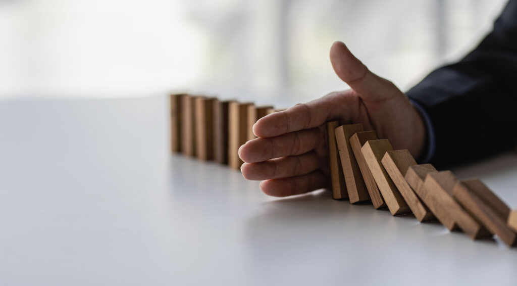 Businessman stops her hand blocking or falling dominoes Financial business and risk management Businessman prevents wooden blocks from falling with his hands